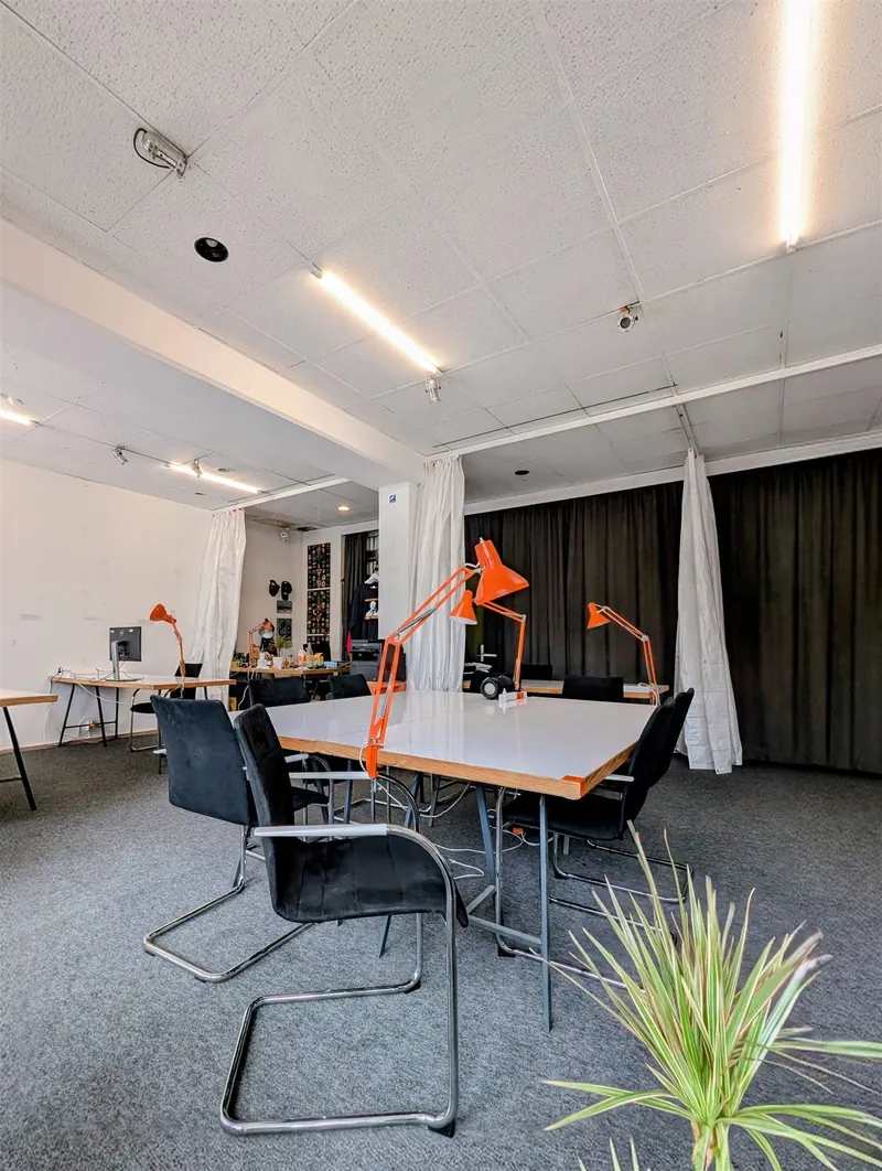 Bright coworking room with a long table, black chairs, orange desk lamps and dark curtains at Kottbusser Tor, Berlin