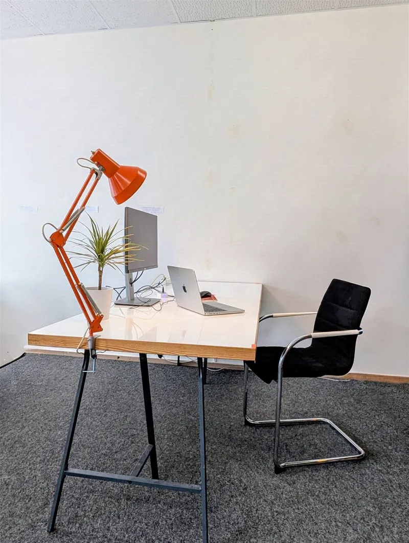 Single desk workspace with monitor, laptop and orange desk lamp in the coworking space